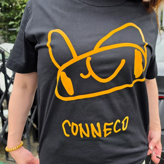 Conneco（こねこ）のマスコット、ラフィちゃんがプリントされた黒いTシャツ。黄色い線画のラフィちゃんの下に、手書き文字で CONNECO